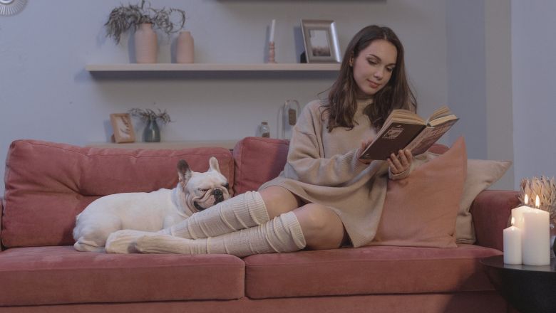 Devojka čita knjigu, a pas spava na kauču
